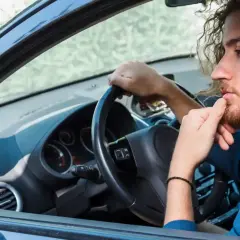 Hombre con barba y pelo rizado, pensativo, con la mano en la barbilla, mientras gira el volante y escucha un **ruido clack clack al girar el volante en parado**.