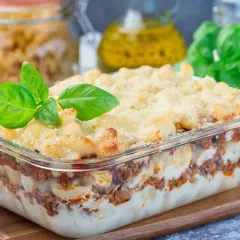 Zapiekanka makaronowa z mięsem mielonym w sosie śmietanowym, udekorowana bazylią. Pyszne danie w szklanym naczyniu.