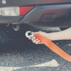 Ręka mocuje hak holowniczy do linki, przygotowując auto do holowania.