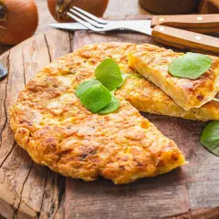 Goldbraune Tortilla de Patatas, garniert mit frischen Blättern, auf rustikalem Holzbrett. Dazu Zwiebeln und Besteck.