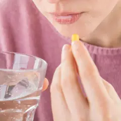 Frau nimmt Kapsel mit Wasser ein, hofft auf Linderung von Tinnitus durch Ashwagandha.
