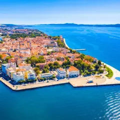 Widok z lotu ptaka na zabytkowe miasto Zadar z czerwonymi dachami, otoczone błękitnym morzem.