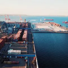 Ogromny port morski z kontenerami i dźwigami, gotowy do eksportu towarów. W oddali widać statek.