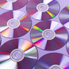 Płyty CD ułożone na fioletowym tle, odbijające światło.