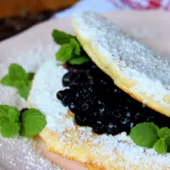 Puszysty omlet z borówkami, posypany cukrem pudrem i udekorowany listkami mięty. Idealny na słodkie śniadanie.