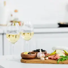 Due calici di vino bianco, ideali come vino bianco per cucinare, accompagnano un tagliere con formaggio, fichi, salumi e olive.