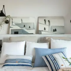 Ideas para hacer un cabecero: dos cuadros de tejados blancos, lámparas negras y cojines a rayas sobre una cama.