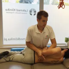 Fizjoterapeuta wykonuje manipulację kręgosłupa pacjenta leżącego na kozetce.