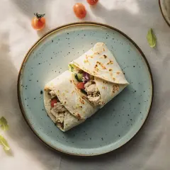Pyszny snack wrap z kurczakiem i warzywami na talerzu, otoczony pomidorkami i listkami.