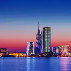 Widok na nowoczesną panoramę Batumi, stolicę Adżarii, o zachodzie słońca. Błyszczące wieżowce i diabelski młyn odbijają się w spokojnej wodzie.