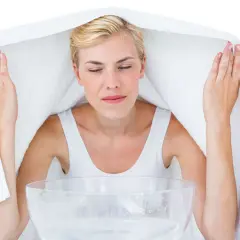 Kobieta z zamkniętymi oczami wykonuje inhalację nad miską z gorącą wodą, przykryta ręcznikiem.
