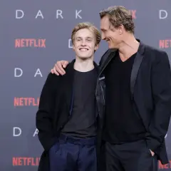 Uśmiechnięty młody aktor z serialu "Dark" i starszy kolega z obsady pozują na tle logo Netflix.