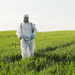 Rolnik w kombinezonie ochronnym i masce przeprowadza fumigację na zielonym polu.
