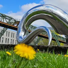 Moderne Skulptur vor Schwebebahn und Gebäude in Wuppertal. Ein Handy zeigt eine Tour durch Barmen, ein tolles Ziel für Ausflugsziele Wuppertal.