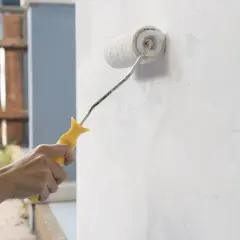 Mano aplica imprimación blanca a una pared con un rodillo. Se puede dar imprimación encima de pintura para un mejor acabado.