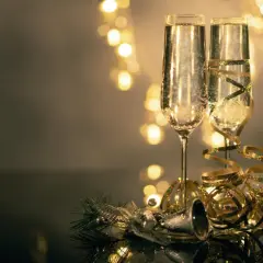 Deux flûtes de champagne pétillant, décorées de rubans dorés, prêtes pour organiser une soirée de nouvel an. Lumières festives en arrière-plan.