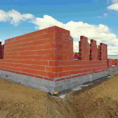 Budowa domu w toku: czerwone ściany z pustaków i betonowy fundament. Zastanawiasz się, ile trwa budowa domu?