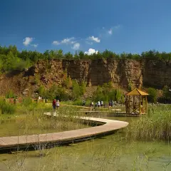 Malowniczy park w Jaworznie z drewnianą kładką wijącą się nad wodą, skalnym zboczem i altanką.