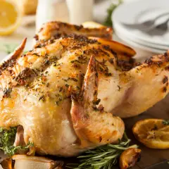 Un délicieux poulet à la broche, doré et savoureux, garni d'herbes fraîches et de quartiers de citron grillés sur une planche en bois.