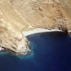 Vista aérea de la playa del medio, una cala rocosa con aguas azules profundas y senderos en las laderas áridas.