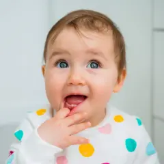 Bambino con dentizione neonato sintomi, che si porta il dito alla bocca con un'espressione curiosa.