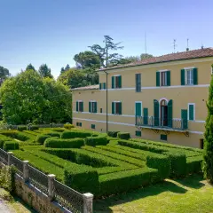 Villa Gracciano della Seta: un giallo edificio con un giardino geometrico di siepi verdi e un cipresso slanciato.