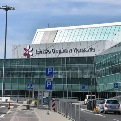 Nowoczesny budynek Lotniska Chopina w Warszawie z charakterystycznym logo. Samochody podjeżdżają do terminala.