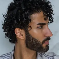 Perfil de hombre con pelo ondulado oscuro y barba cuidada.