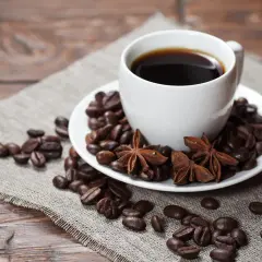 Aromatic czarna kawa właściwości pobudzające, otoczona ziarnami kawy, anyżem i laskami cynamonu na lnianym płótnie.