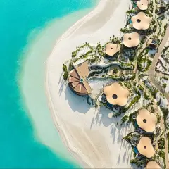 Widok z lotu ptaka na luksusowy hotel Four Seasons z unikalnymi, kwiatowymi dachami, położony przy turkusowym morzu i białej plaży.