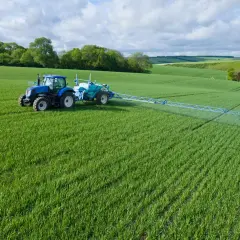 Niebieski traktor z opryskiwaczem na zielonym polu.