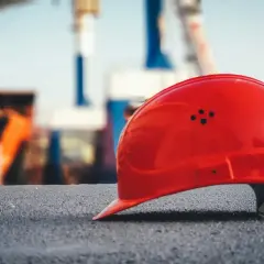 Czerwony kask fgśp leży na szarej nawierzchni, w tle widać budowę z maszynami i konstrukcjami.
