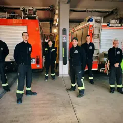 Sechs Männer in Einsatzkleidung stehen vor zwei Feuerwehrautos. Sie leisten ehrenamtlich Dienst bei der Feuerwehr und sind bereit für den nächsten Einsatz.