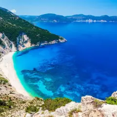 Widok na Myrtos, jedną z najpiękniejszych plaż i głównych **kefalonia atrakcje**. Biały piasek, turkusowa woda i strome klify.