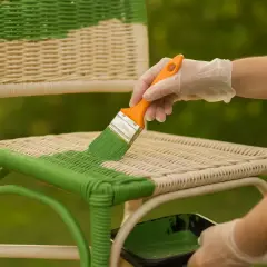 Osoba w rękawiczkach maluje zieloną farbą rattanowe krzesło. To świetny sposób, by odświeżyć meble i dowiedzieć się, czym pomalować rattan.
