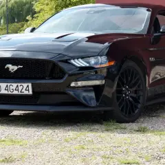 Czarny Ford Mustang z polską tablicą rejestracyjną stoi na żwirowej nawierzchni.