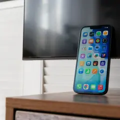 Nowy iPhone z ekranem pełnym ikon, gotowy do nagrywania rozmów. Obok czarny ekran telewizora.