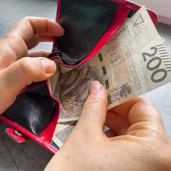 Dwie ręce wkładają banknot 200 zł do czerwonego portfela. Czy kosiniakowe wlicza się do dochodu?