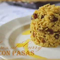 Arroz al curry con pasas, un plato aromático y dulce servido en un plato blanco con un toque de salsa dorada.