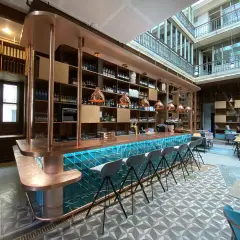 Le bar moderne du "Le Shack Paris" avec son comptoir en cuivre et ses tabourets gris, baigné de lumière naturelle.