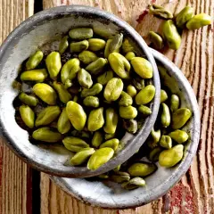 Grüne Pistazienkerne in zwei Schalen auf Holzuntergrund. Sie sind ein gesunder Snack, der viele Nährstoffe liefert.