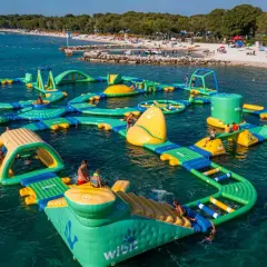 Wodne miasteczko z dmuchanymi atrakcjami w bi village camping. Dzieci i dorośli bawią się na ślizgawkach i trampolinach w morzu.