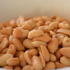 Un cuenco blanco lleno de cacahuetes o maní tostados, listos para ser disfrutados como un snack saludable.