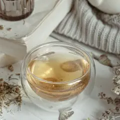Ciepła, aromatyczna biała herbata w szklance, otoczona suszonymi ziołami i książką. Idealny moment na relaks.