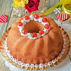Delicioso bizcocho con forma de anillo, decorado con crema, cerezas y corazones. Un dulce baba al ron perfecto para celebrar.