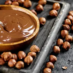Schokocreme selber machen: Eine Schüssel voller cremiger Schokocreme neben gerösteten Haselnüssen auf einem Holzbrett.