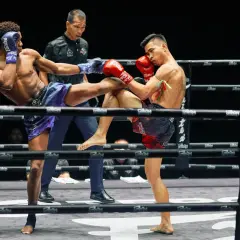 Två thaiboxare i full action i Lumpinee Stadium. En spark möter ett block.
