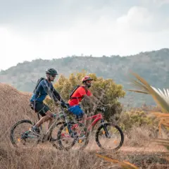 Dos ciclistas disfrutan de rutas en bici para principiantes en un paisaje rural con colinas y vegetación seca.