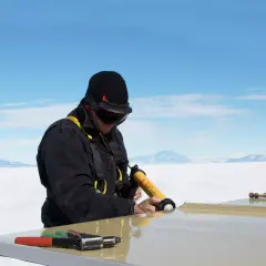 Hombre con equipo de seguridad usa pistola aplicadora de **productos químicos** para sellar una superficie en un paisaje nevado.