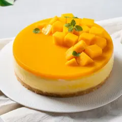 Sernik z błyszczącą polewą mango, ozdobiony kostkami mango i listkami mięty.